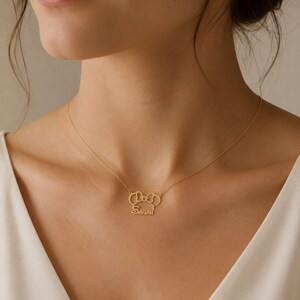 May include: A gold-toned necklace featuring a pendant shaped like a stylized mouse head with a bow on top. The name Sarah is written in cursive script across the bottom of the mouse head design. The pendant is attached to a thin, delicate gold chain.