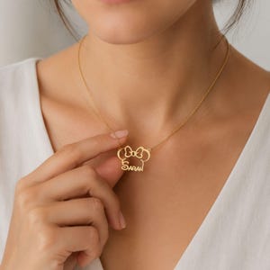 May include: A gold-toned necklace featuring a pendant with a stylized mouse ear silhouette topped with a bow, incorporating the name SARAH in a cursive script font. The pendant is attached to a delicate gold-toned chain that rests around the neck.