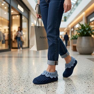 May include: A pair of dark navy blue ribbed knit slippers featuring a light blue scalloped crochet trim around the ankle opening. The slippers are worn with dark blue denim jeans that are cuffed at the bottom, showcasing the textured knit design.