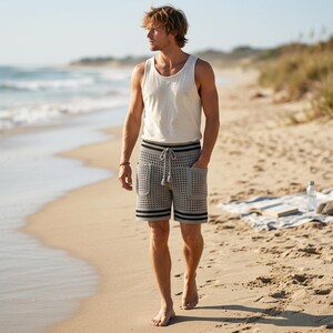 May include: A cream-colored sleeveless tank top and light gray crochet shorts featuring a grid pattern, two front patch pockets, a drawstring waist with tassels, and horizontal black stripes along the waistband and the bottom hem of the shorts.