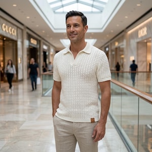 May include: A short-sleeved, off-white polo shirt featuring a textured, open-knit pattern, a classic collar, and a V-neck opening. The shirt is paired with light beige trousers and includes a small, square brown label at the bottom hem.