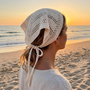 May include: An off-white crochet headscarf featuring a triangular shape with an intricate openwork diamond pattern. The headscarf is secured at the back of the head with two long, matching crocheted ties that are knotted into a bow.
