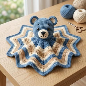 May include: A crochet security blanket featuring a blue bear head with black eyes and a stitched nose. The blanket body is star-shaped with concentric chevron stripes in shades of blue, beige, and cream, creating a textured, soft, and layered appearance.