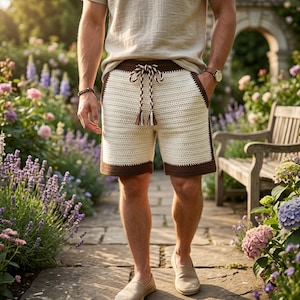 May include: Crochet shorts featuring a cream-colored main body with dark brown trim along the hem and waistband. The shorts include a thick, braided drawstring in matching cream and brown tones with tassel ends, and two side pockets.