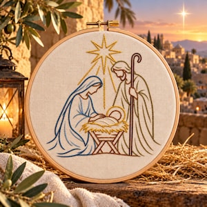 May include: A circular wooden embroidery hoop containing a fabric panel with a stitched nativity scene. The design features a figure in blue robes, a figure in tan robes with a staff, and a baby in a manger under a yellow star.