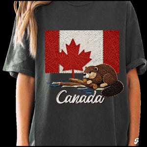 Può includere: Una t-shirt grigio antracite con un design grafico della bandiera canadese in stile string art. Sotto la bandiera c'è un castoro marrone appoggiato su un tronco, con la parola Canada scritta in un carattere corsivo bianco sotto.