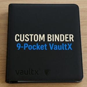 Op de afbeelding: Een zwarte rechthoekige map met een gladde afwerking. De voorkant bevat de tekst CUSTOM BINDER in het wit en 9-Pocket VaultX in het blauw. Het onderste gedeelte van de kaft toont de in reliëf aangebrachte merknaam vaultx en een schildje.