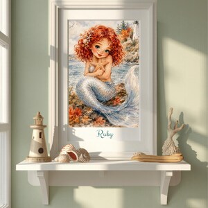 Könnte beinhalten: Ein gerahmter Kunstdruck mit einer Illustration einer Meerjungfrau mit lockigem rotem Haar, die einen Seestern hält, vor einer Küstenkulisse mit einem Leuchtturm. Der Name Ruby ist in blauer Schreibschrift am unteren Rand abgedruckt.