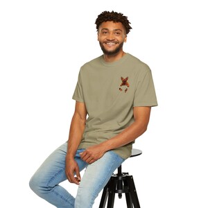 Può includere: Una t-shirt a maniche corte color verde oliva chiaro con una piccola grafica di un bulldog francese marrone sul lato sinistro del petto. La maglia presenta un girocollo e una vestibilità standard, realizzata in tessuto a tinta unita.