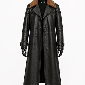 Puede incluir: Una gabardina larga de cuero negro con cuello de piel sintética marrón, cierre frontal de doble botonadura y correas con hebilla ajustables en los puños. El abrigo se muestra en un maniquí negro con camisa y pantalones de color negro.