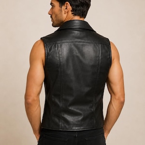 May include: A black sleeveless leather vest featuring a wide collar, vertical seam detailing on the back, and a fitted silhouette. The garment is constructed with a smooth finish and is worn over black pants, showcasing a clean and structured design.