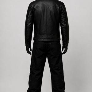 May include: A black leather jacket with a high collar and vertical seam detailing on the back, paired with black trousers featuring side pockets and metallic rivets. The outfit is displayed on a black mannequin against a neutral background.