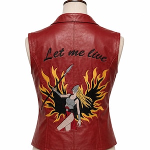 May include: A red sleeveless waistcoat featuring a collar and a large embroidered graphic on the back. The embroidery depicts a warrior figure with long blonde hair holding a spear, surrounded by black and yellow flames, with the text Let me live.