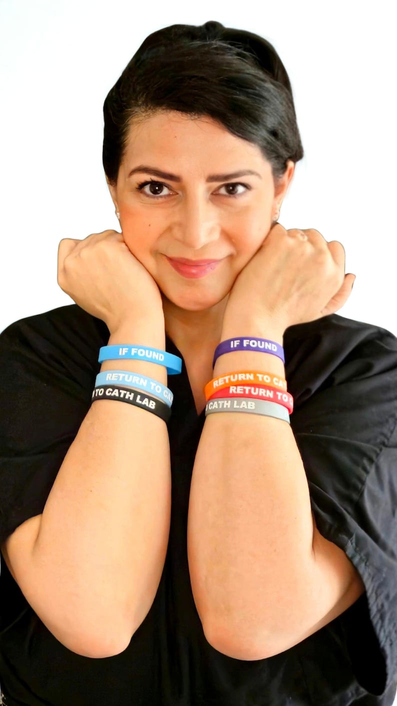 Puede incluir: Un conjunto de seis pulseras de silicona que se llevan en los antebrazos. El brazo izquierdo tiene pulseras azul claro, blancas y negras, mientras que el derecho tiene pulseras moradas, naranjas y grises. Cada una lleva el texto IF FOUND RETURN TO CATH LAB.