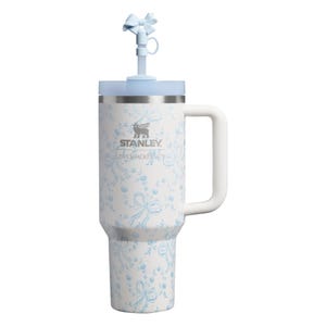 Puede incluir: Un vaso t&eacute;rmico blanco con un patr&oacute;n de lazos y flores azul claro, que cuenta con un asa lateral, una tapa azul claro y una pajita rematada con un accesorio de lazo azul claro. Los logotipos de Stanley y LoveShackFancy est&aacute;n impresos en plata.