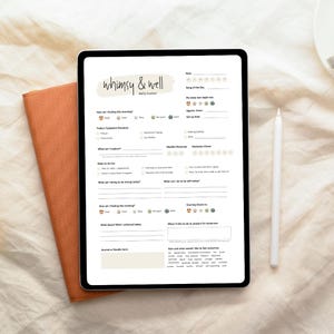 May include: A digital tablet displaying a "whimsy & well" daily tracker. The tracker includes sections for mood, symptoms, and daily goals. A white stylus rests beside the tablet, and a burnt orange notebook is visible on the left.