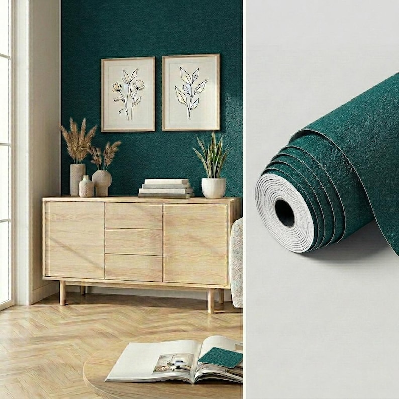 May include: A roll of dark teal wallpaper with a textured surface shown next to a light wood sideboard featuring three drawers and two cabinets, positioned against a matching dark teal wall with two framed botanical line art prints.