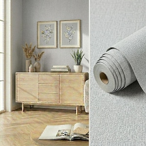 May include: A roll of light gray wallpaper with a textured, fabric-like surface pattern. The wallpaper features a subtle, woven appearance that mimics the look of linen, providing a neutral and consistent finish for interior wall applications.