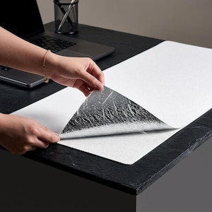 May include: A rectangular desk mat with a textured white top surface and a reflective silver metallic underside. The mat is partially lifted to reveal the contrasting silver material, showcasing its dual-layered construction and smooth edges.