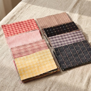 May include: A collection of rectangular fabric swatches arranged in two stacks. The patterns include red and white gingham, pink dashed lines, textured rose, yellow floral grid, tan plaid, black with small squares, purple plaid, and dark navy grid.