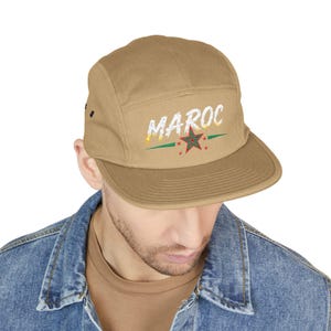 Peut inclure: Casquette cinq panneaux beige avec le mot "MAROC" en blanc, avec une étoile et des accents verts et jaunes. La casquette a une visière plate et une fermeture à pression noire à l'arrière.