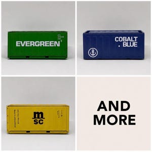 Könnte beinhalten: Drei rechteckige Schiffscontainer-Modelle in Grün, Blau und Gelb. Der grüne Container trägt den Schriftzug EVERGREEN. Der blaue Container zeigt den Text COBALT BLUE und ein Ankersymbol. Der gelbe Container zeigt den Text msc.