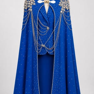 May include: A royal blue cape and matching blazer set featuring scattered silver rhinestones, silver chain embellishments draped across the front, and large decorative crystal clusters on the shoulders. The cape has a white collar clasp.