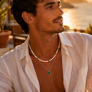 Peut inclure: Un ensemble de colliers à deux rangs. Le rang supérieur est composé de perles blanches et de perles vertes. Le rang inférieur est une chaîne en argent avec un pendentif vert carré. La personne porte une chemise blanche boutonnée.