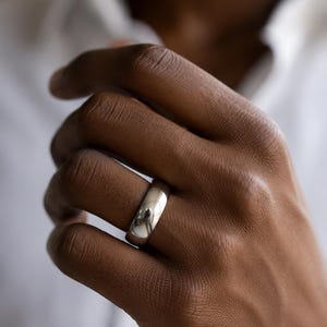 Peut inclure: Une bague en métal argenté poli avec un anneau lisse et arrondi doté d'une surface réfléchissante très brillante. La bague présente une construction simple et solide avec un profil bombé qui entoure le doigt, offrant une finition métallique uniforme.