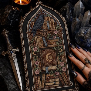 May include: A gothic-style arched cross-stitch embroidery featuring a black raven perched atop a bookshelf filled with various books, accented by pink roses and a central crescent moon motif, all framed in an ornate, antique-gold metal border.
