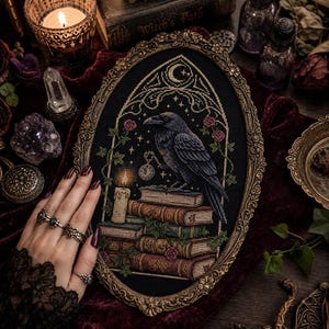 May include: An oval-framed cross-stitch embroidery featuring a black raven perched on a stack of books. The design includes a lit candle, a crescent moon, stars, and small pink roses, all set against a black fabric background within an ornate gold frame.