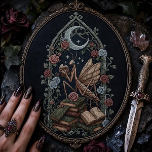 May include: An oval-framed cross-stitch embroidery on black fabric featuring a praying mantis reading a book atop a stack of books. The scene is framed by an arched trellis of roses and vines under a crescent moon, rendered in shades of brown, green, and red.