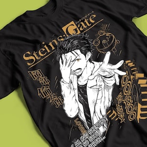 May include: A black t-shirt featuring a graphic print of an anime character with dark hair, wearing a lab coat, with one hand covering their face. The design includes the text Steins;Gate, Japanese characters, a gear, and the phrase I AM MAD SCIENTIST.