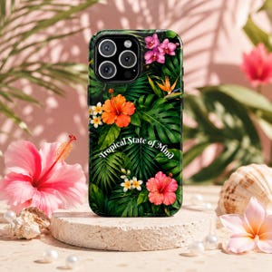Puede incluir: Una funda de smartphone negra con un vibrante estampado tropical de hojas de palmera verde oscuro, flores de hibisco de color naranja y rosa brillante, y pequeñas flores blancas. El texto Tropical State of Mind está impreso en blanco en el centro.