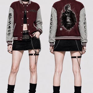May include: A maroon and gray varsity jacket featuring white striped ribbed cuffs and collar. The right sleeve displays vertical text, while the back showcases a graphic print of a person with Korean text. The jacket is worn over a black crop top and skirt.