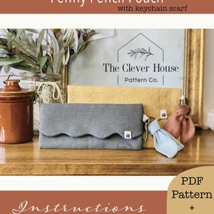 May include: A gray pencil pouch with a scalloped flap and a small house logo tag, positioned in front of a mustard yellow pouch. Both feature metal lobster clasps with small fabric scarf attachments in light blue and dusty rose colors.
