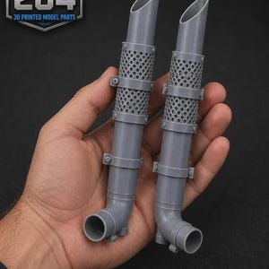 May include: Two grey 3D printed model exhaust pipes featuring a cylindrical shape with angled cut tops, perforated heat shield sections, and circular mounting brackets. The pipes have a smooth finish and include a logo reading PRINT THAT 204.