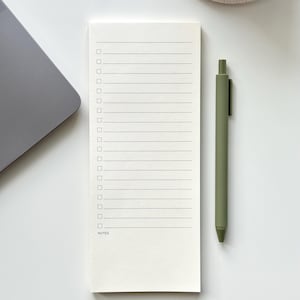 May include: A rectangular off-white notepad featuring a vertical checklist with seventeen horizontal lines, small square checkboxes, and the word NOTES printed at the bottom, accompanied by a matte olive green retractable ballpoint pen.