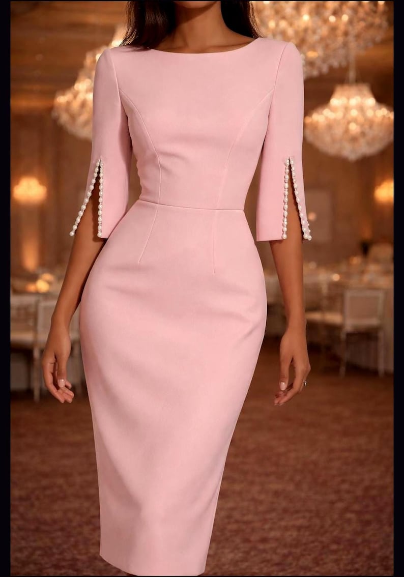 May include: A light pink knee-length dress featuring a boat neckline, fitted bodice, and three-quarter length sleeves. Each sleeve has a vertical slit detail along the outer arm, embellished with a single row of small white pearls along the edges.