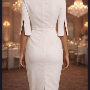 May include: A white knee-length sheath dress featuring a boat neckline, elbow-length sleeves with vertical side slits, and a row of small white buttons lining each sleeve opening. The dress has a fitted silhouette with a center back zipper closure.