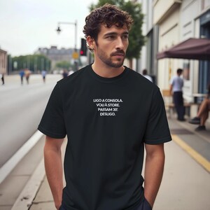Könnte beinhalten: Ein schwarzes kurzärmeliges T-Shirt mit weißem Text auf der Brust, der lautet: LIGO A CONSOLA. VOU À STORE. PASSAM 30'. DESLIGO. Das Kleidungsstück hat einen Rundhalsausschnitt und eine Standardpassform aus einfarbigem schwarzem Stoff.