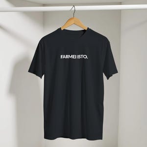 Op de afbeelding: Een zwart T-shirt met korte mouwen en de witte tekst FARMEI ISTO. op de borst gedrukt. Het kledingstuk hangt aan een houten kleerhanger en heeft een ronde halslijn en een standaard pasvorm, uitgevoerd in een effen zwarte stof.