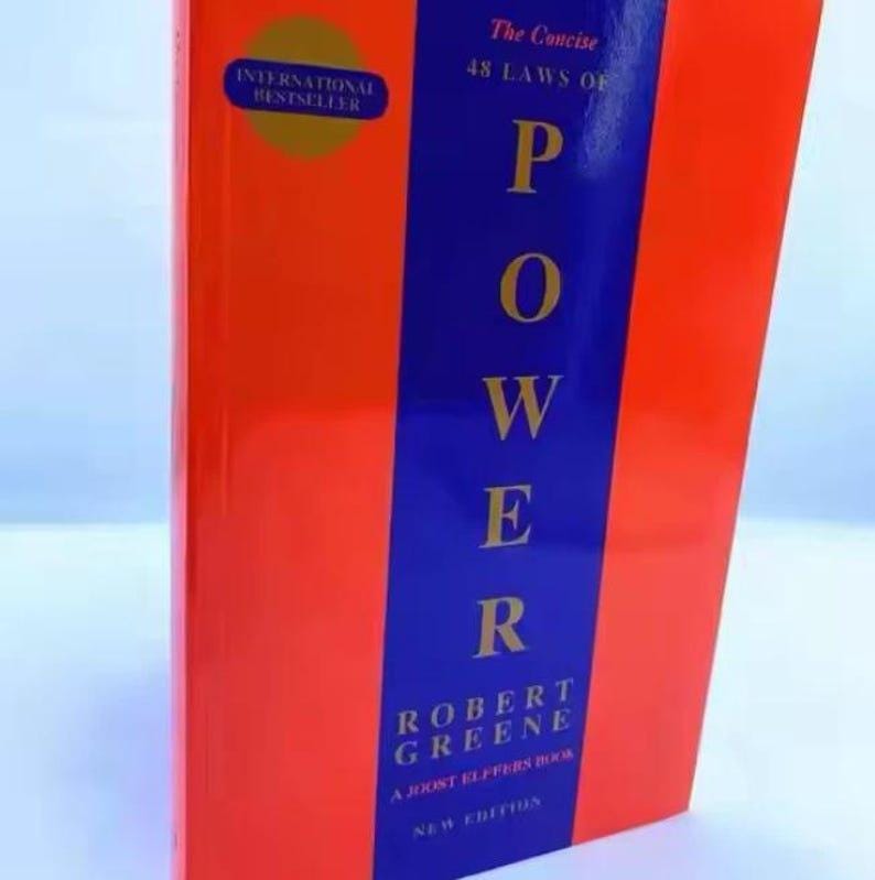 Op de afbeelding: Een hardcover boek getiteld "POWER" van Robert Greene. Het boek heeft een rode kaft met een blauwe verticale streep. Het woord "POWER" staat prominent in grote witte letters. Het boek is een internationale bestseller.