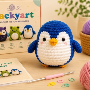 K&ouml;nnte beinhalten: Ein handgeh&auml;kelter Pinguin in Blau und Wei&szlig; mit gelbem Schnabel und F&uuml;&szlig;en. Das Bild zeigt auch ein H&auml;kelset f&uuml;r Anf&auml;nger mit dem Wort "Packyart" auf der Box und einer Schritt-f&uuml;r-Schritt-Anleitung. Weitere geh&auml;kelte Tiere sind ebenfalls zu sehen.