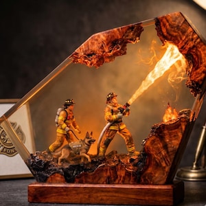 Könnte beinhalten: Eine dekorative Harz- und Holzlampe mit zwei Feuerwehr-Miniaturen in gelber Schutzkleidung, von denen eine einen Schlauch mit leuchtendem Flammeneffekt hält, begleitet von einem Deutschen Schäferhund mit einer Weste mit der Aufschrift MICH M.