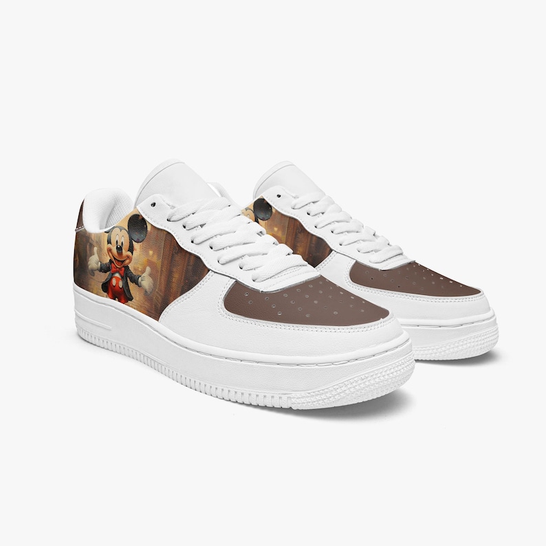 May include: A pair of white sneakers featuring a brown toe box and a side panel graphic of a cartoon mouse character wearing a red jacket and bowtie. The shoes have white laces, a white midsole, and a white outsole with a classic low-top silhouette.