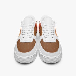 May include: A pair of low-top sneakers featuring a white base with white laces and a brown toe box. The side panels display a brown and orange patterned design. The shoes have a perforated toe area and a thick white rubber sole with a textured tread.