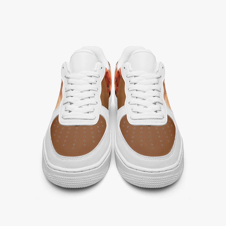 May include: A pair of low-top sneakers featuring a white base with white laces and a brown toe box. The side panels display a brown and orange patterned design. The shoes have a perforated toe area and a thick white rubber sole with a textured tread.