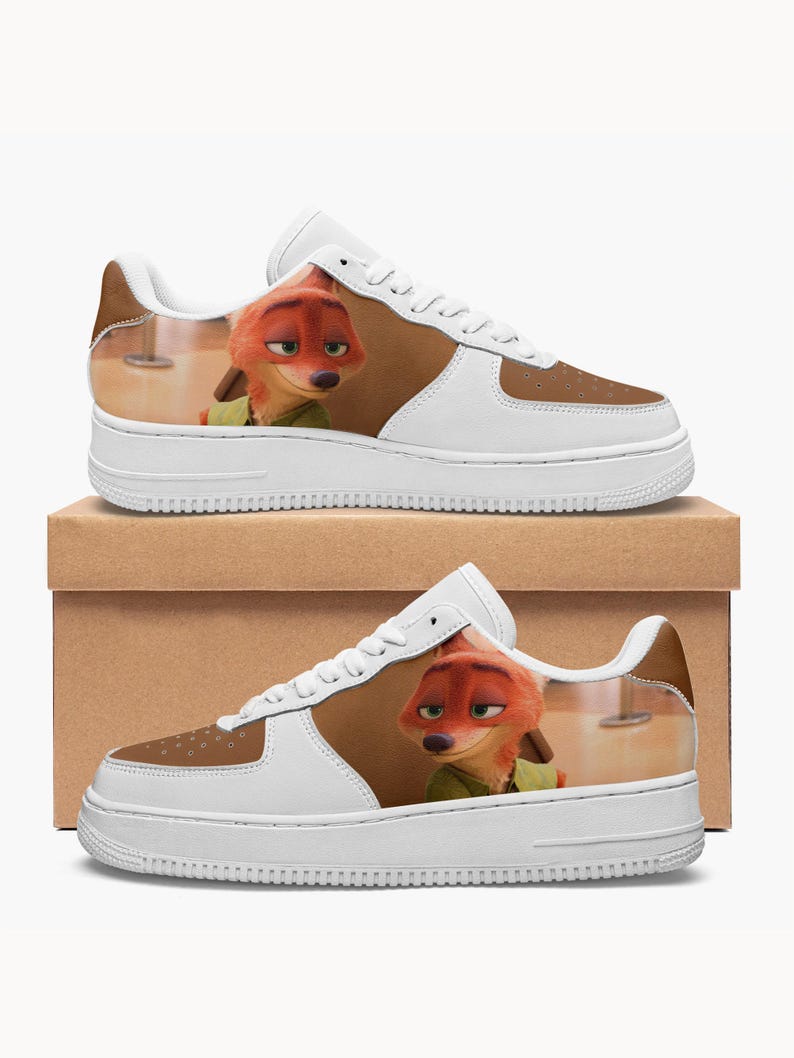May include: A pair of white sneakers featuring a printed graphic of the animated fox character Nick Wilde from Zootopia. The shoes have white laces, a white sole, and brown panels on the toe and side, showcasing the character's orange fur and green shirt.