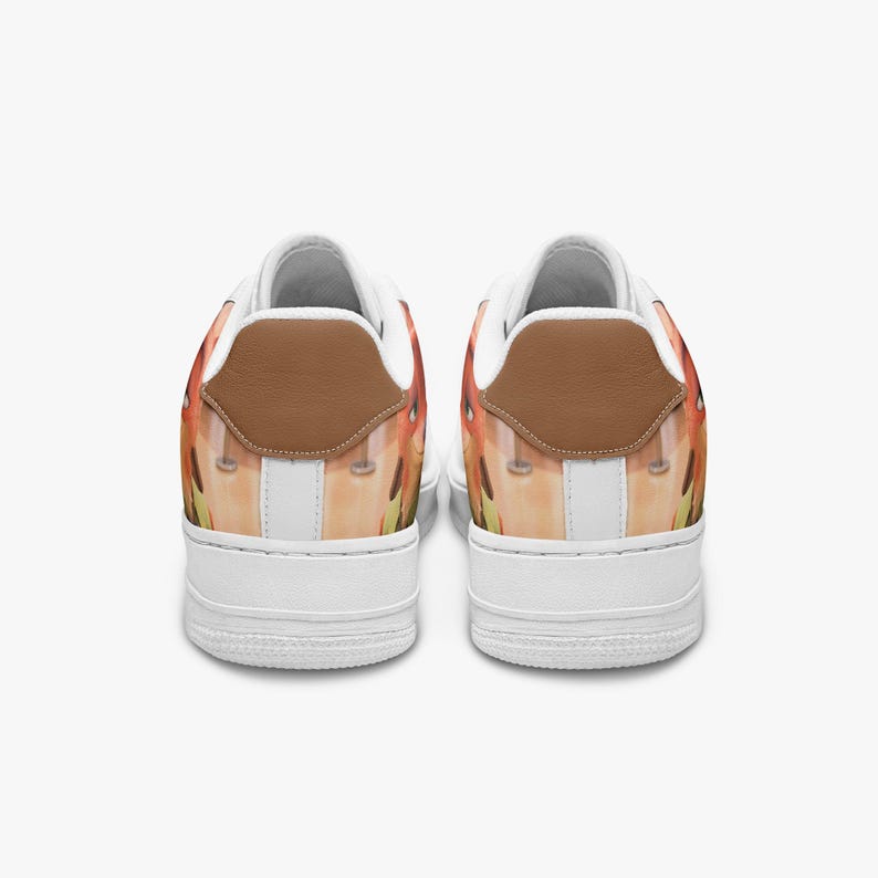 May include: A pair of low-top sneakers featuring a white rubber sole and a brown leather heel tab. The upper portion of the shoes displays a printed graphic with orange, yellow, and tan tones, complemented by white interior lining and white laces.